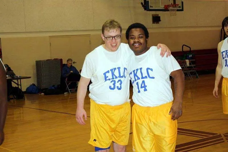 Two Heroes in matching basketball jerseys with their arms around each other, smiling on the court.